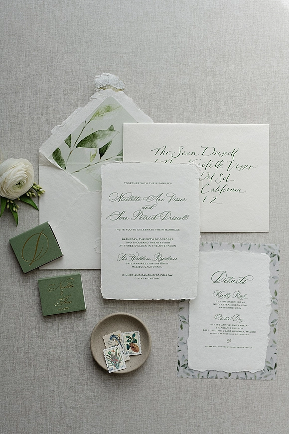 Invitation suite with deckle edge wedding invitations, calligraphy envelopes, wax seal, vintage stamps and ranunculus on linen backdrop