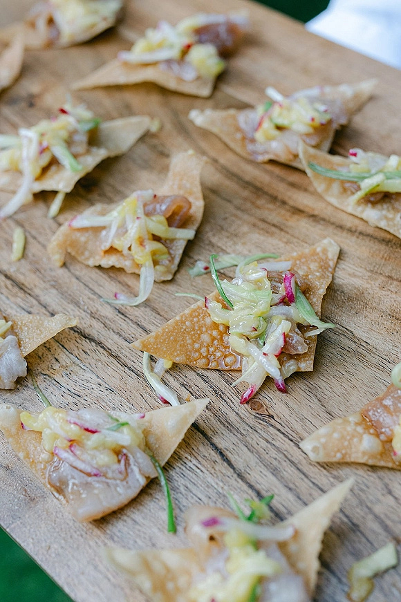 Wedding appetizers arranged as passed hors d'oeuvres on a wooden serving board, crispy wonton chips topped with slaw on a tabletop