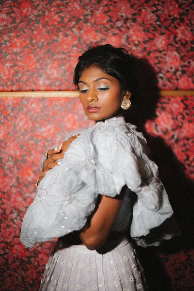Bridal portrait of a bride in a sequin puff sleeve wedding dress looking down over her shoulder against patterned wallpaper and a red wall shadow