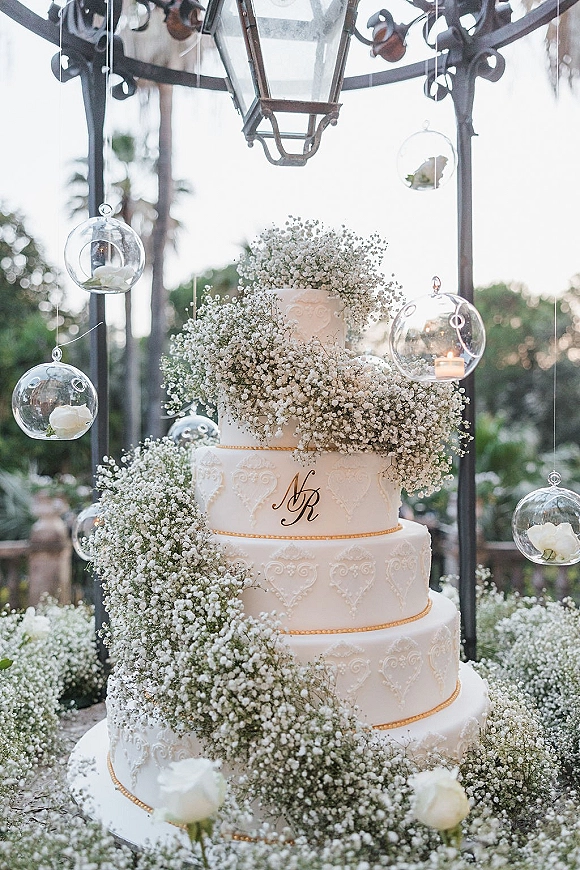 Wedding cake four tier wedding cake with embossed icing, monogram initials and gold trim, adorned with baby's breath and roses in a garden setting