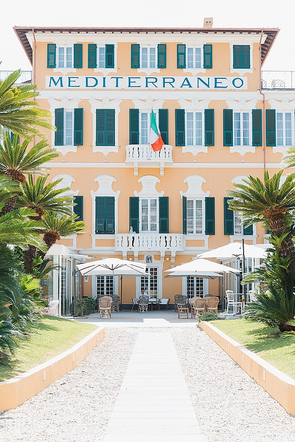 Wedding venue exterior with cafe tables and patio umbrellas outside a hotel wedding venue, framed by palm trees and a peach stucco facade