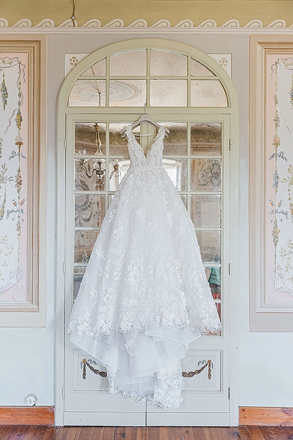 Wedding dress with lace wedding dress bodice, V-neck and spaghetti straps on a hanger before an arched windowed door, airy tulle skirt