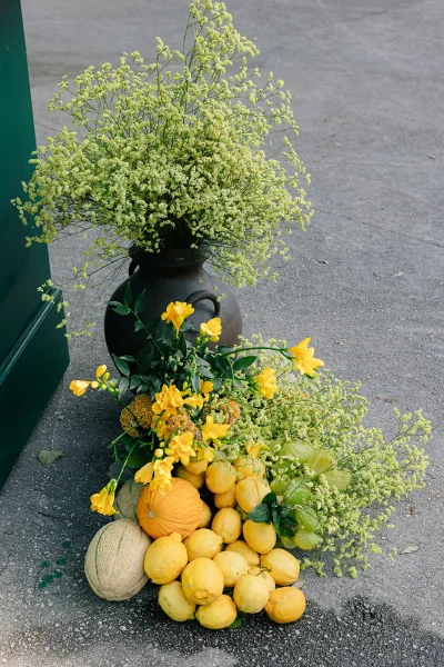Wedding floral arrangement in citrus wedding decor, lemons tucked among lush blooms, set against a green painted wall outdoors.