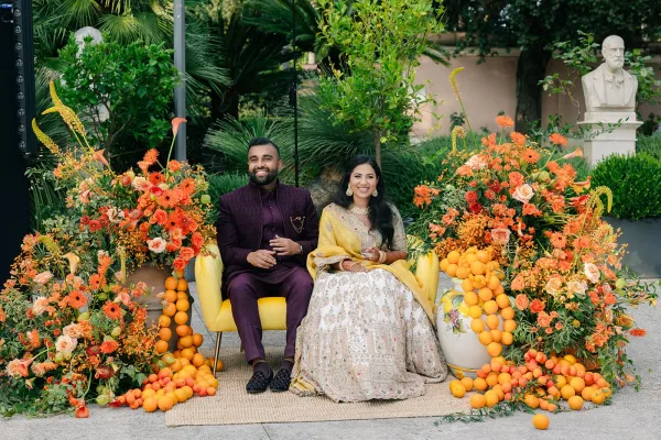 Couple portrait framed as an Indian wedding portrait, bride with a yellow dupatta beside her groom, amid garden palms.
