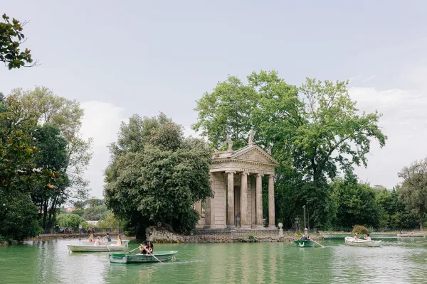 Lakeside temple, a neoclassical pavilion, stands on the shore, with rowboats drifting nearby and trees mirrored on the calm lake.