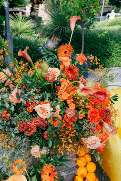 Wedding floral arrangement styled as citrus wedding decor, vibrant blooms with oranges on a stone path amid lush garden greenery.