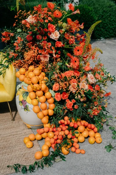 Wedding floral installation with citrus wedding decor in a ceramic urn, set beside a yellow chair on a jute rug.