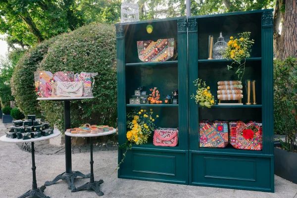 Wedding favor display doubling as a welcome bag display with a decorative birdcage, framed by garden trees and a sunlit stone path.