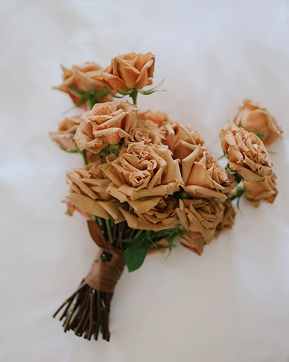 Rose bouquet with roses and greenery, ribbon-wrapped stems arranged on a white fabric backdrop, styled as a beige rose bouquet flat lay