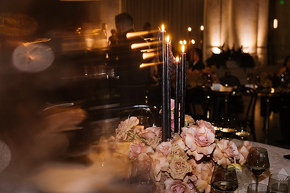 Reception centerpiece with tall taper candle centerpiece featuring black taper candles and pink roses on a set table in a dim room