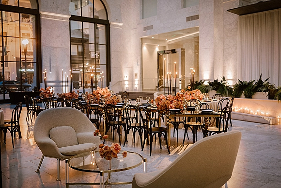 Reception tablescape with wedding reception table decor, peach rose centerpieces, taper candles and greenery garland on a long gold table by arched windows