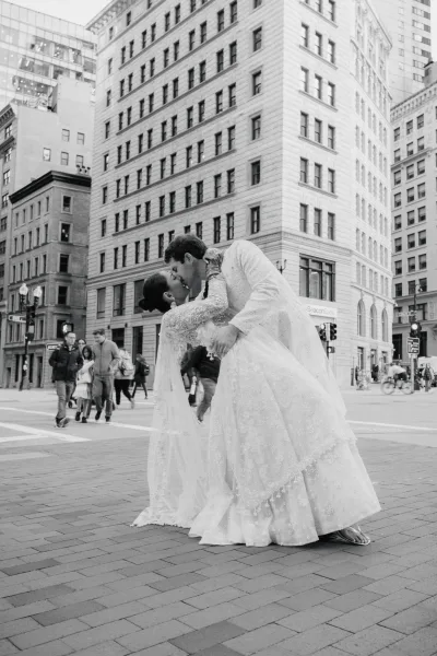 Wedding kiss portrait of groom dipping the bride as they kiss, her lace long-sleeve dress and veil flowing in a busy city crosswalk