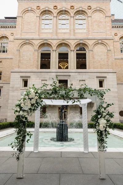 Wedding ceremony arch with greenery wedding arch garland, white roses and hydrangeas, draped fabric, set by a courtyard fountain and stone facade