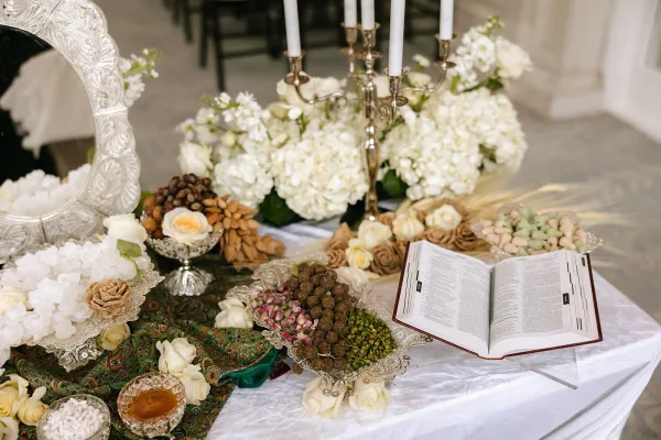 Sofreh aghd setup for a Persian wedding ceremony table, centered around a mirror and arranged with traditional ceremonial elements, by wall molding.