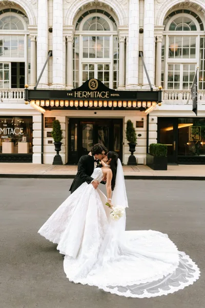 Wedding kiss portrait capturing a dip kiss wedding photo as the groom dips his bride with a long train beneath a hotel marquee.