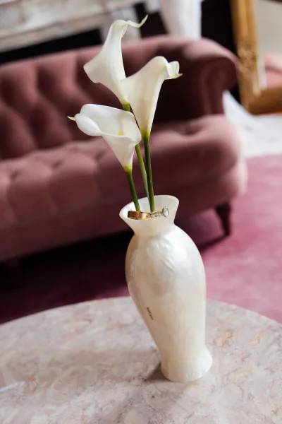 Wedding ring detail with an engagement ring photo styled on a marble tabletop, with a tufted sofa and pink rug framing a fireplace mantel.