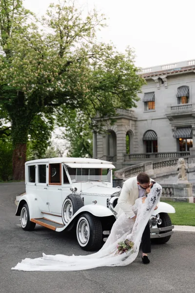 Wedding kiss portrait with the groom dipping the bride, her lace gown sweeping the stone staircase before a grand mansion facade.
