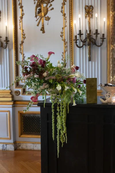 Wedding floral arrangement in an asymmetrical floral design with trailing greenery, set against gilded molding and white paneled walls.