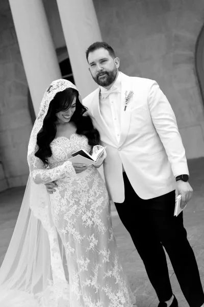 Couple portrait featuring a bride in lace gown with mantilla veil, close to her groom, framed by stone columns and a weathered archway.
