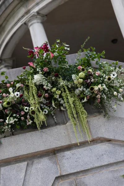 Wedding floral installation with architectural floral decor and hanging amaranthus, cascading around a stone archway and columns.