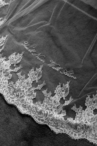 Wedding veil detail of a lace bridal veil featuring delicate embroidered script, draped over textured dark fabric.