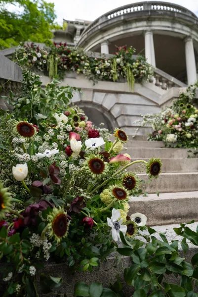 Wedding staircase flowers and ceremony entrance flowers cascade in floral garlands over stone steps and balustrade at a historic building.