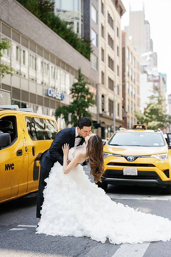 Wedding kiss portrait of bride and groom kiss in a crosswalk, her long train flowing as he dips her beside a yellow taxi on a city street