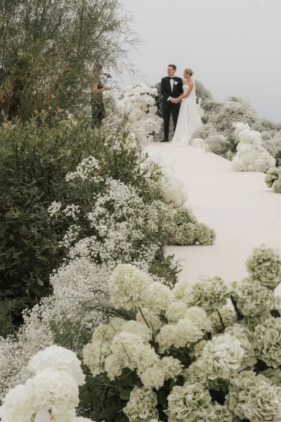 Ceremony moment at an outdoor wedding ceremony with the couple centered on the aisle, framed by baby's breath against garden greenery.
