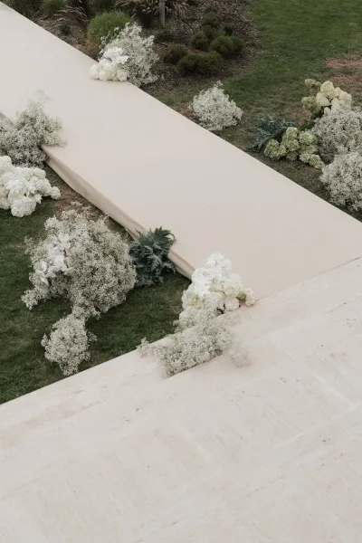Ceremony aisle decor for a garden ceremony aisle, featuring white orchids along a stone terrace path bordered by garden shrubs.
