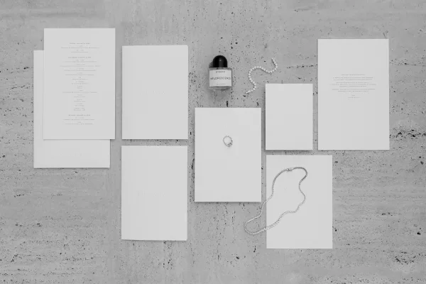Wedding stationery flat lay of an invitation suite featuring a minimalist white design, paired with vow books on a textured stone surface.