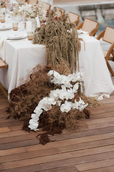 Reception tablescape featuring a white orchid centerpiece and taper candles, set on a wood deck beside the water.