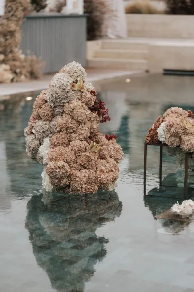 Floral installation for poolside wedding decor, sculptural clusters of billowing hydrangeas, mirrored in the still pool water.