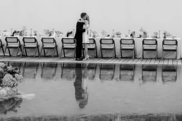 Wedding kiss portrait capturing a couple's embrace moment by a serene pool on a wooden deck, the bride in a chic bridal mini dress.