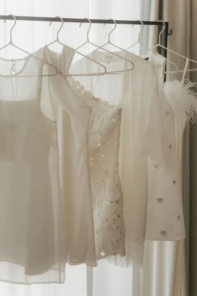 Wedding dress hanging, an ivory bridal gown with delicate lace, softly backlit by sheer curtains at a bright window.