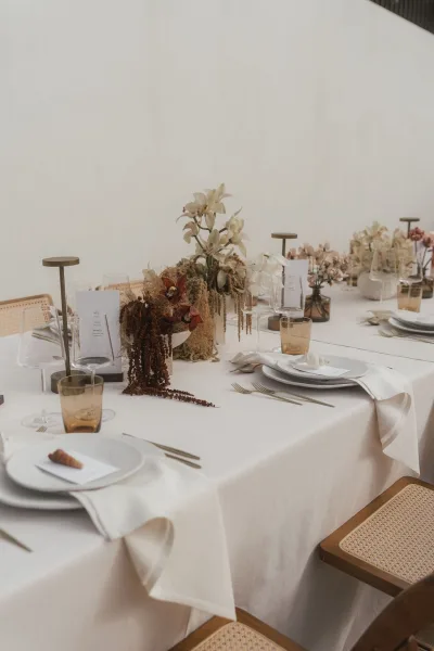 Reception tablescape styled as a minimalist wedding table, highlighted by warm amber glassware amid clean place settings.