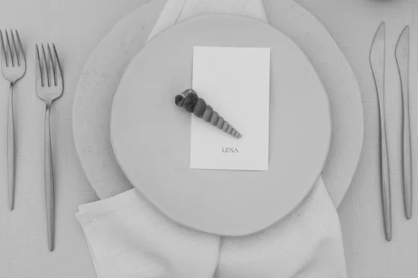 Wedding place setting featuring a seashell place card in a minimalist, coastal-inspired style with modern, understated elegance.