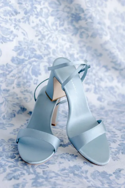 Wedding shoes in something blue, strappy blue high heel sandals with ankle straps resting on blue and white floral fabric backdrop