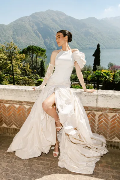 Bridal portrait of a bride on the stone terrace, poised in an ivory gown with a single lace glove, framed by mountains and a lake.