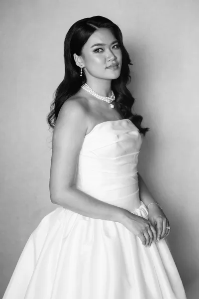 Bridal portrait of a bride in a strapless satin wedding dress with pearl necklace and drop earrings against a plain studio backdrop
