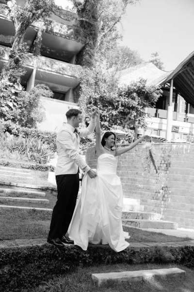 Couple portrait of bride and groom dancing, her strapless gown twirling as he leads her on ivy-covered steps by a brick wall