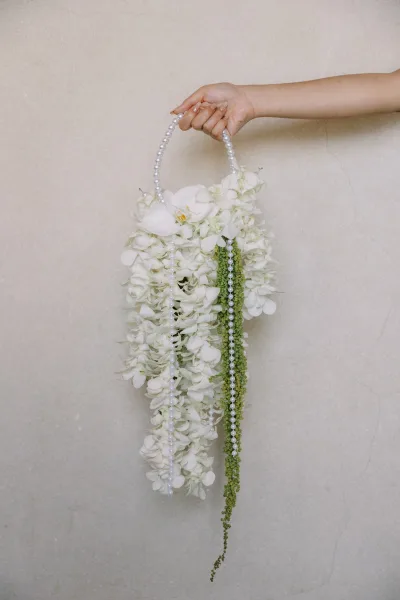 Bridal bouquet with cascading wedding bouquet of white orchids and hanging strands, pearl handle and greenery held against a neutral wall