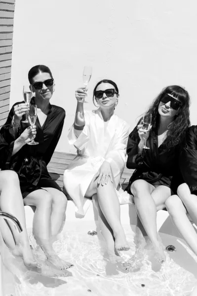 Bridal party toast during the bride getting ready, champagne glasses raised poolside by a hot tub on a wood deck.