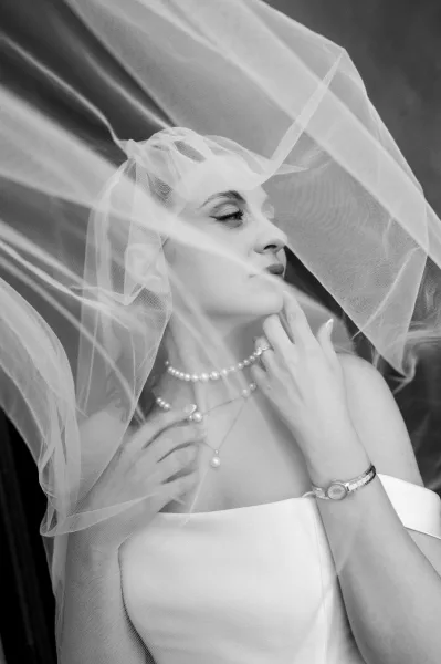 Bridal portrait of a bride under veil, posed with a simple pearl necklace and soft, timeless styling.