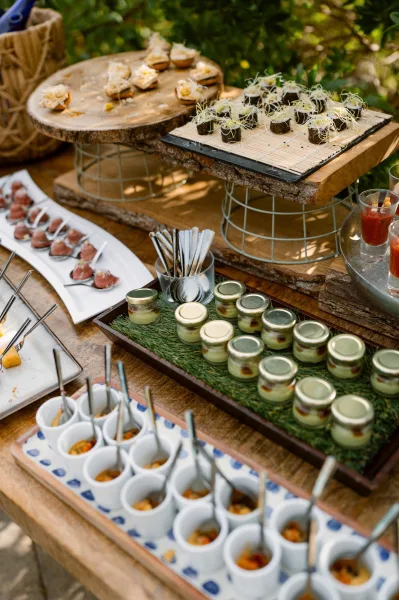Wedding appetizers and cocktail hour bites featuring sushi rolls, arranged on a wooden table against lush garden greenery.