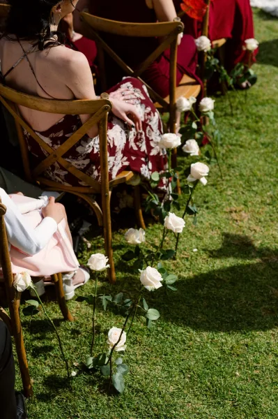 Ceremony aisle flowers arranged as single stem aisle decor with white roses lining a grass lawn walkway for a simple outdoor ceremony