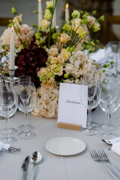 Reception table decor featuring wedding centerpiece flowers and taper candles, with wood chairs and a tree trunk hinting at an outdoor setting.
