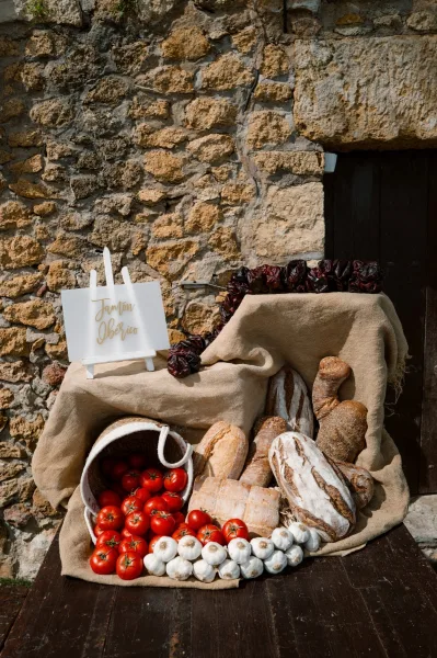 Wedding food display arranged as a rustic grazing station, featuring artisan bread on a wooden table against a stone wall and wooden door.