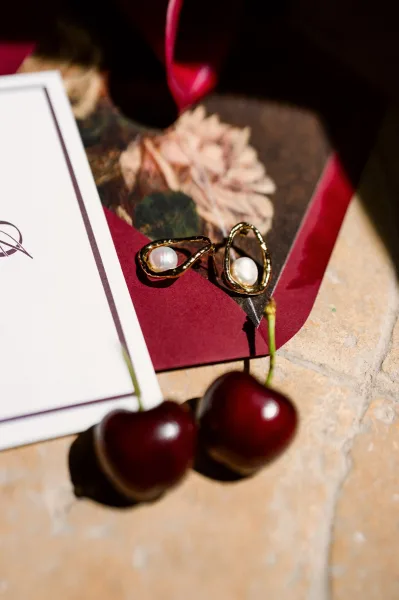 Bridal earrings, delicate pearl drop earrings styled on stone tile with a single cherry accent for a refined flatlay.