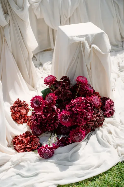 Wedding floral arrangement of burgundy wedding flowers before soft white draped fabric, creating a bold statement against the fabric backdrop.