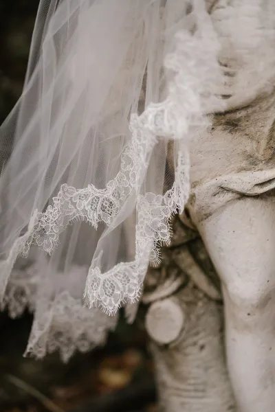 Bridal veil with lace wedding veil trim and sheer tulle fabric draped over a stone statue in an outdoor setting